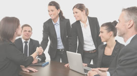 Two Businesswomen Shaking Hands with Four Colleagues Around Meeting Table